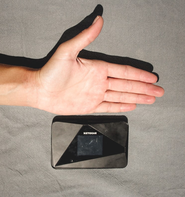 Eine Hand liegt neben einem mobilen Router von Netgear und verdeutlicht, wie handlich ein mobiler Router ist. Es ist eine Möglichkeit, um Internet im Wohnmobil zu haben