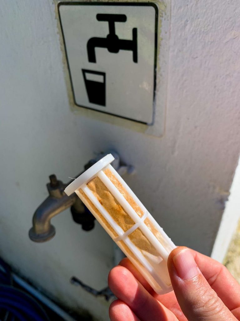 Ein verfärbter Sedimentfilter eines Vorfilters, es hat sich viel Sediment im Filter verfangen, dass ohne den Filter im Frischwassertank des Wohnmobils gelandet wäre. Im Hintergrund sieht man einen Wasserhahn bei dem man sich Frischwasser tanken kann.