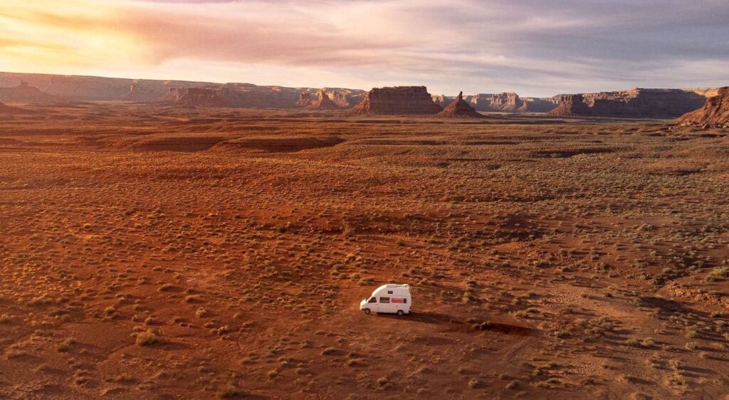 Drohnenaufnahme einer DJI Mavic Mini auf dem ein weißer Mercedes Sprinter in einer kargen Wüstenlandschaft in Utah, in den USA zu sehen ist. Im Hintergrund sieht man weit entfernt rote Felsen. Der Drohnenpilot ist mit der Helden Drohnenversicherung weltweit und somit auch in den USA abgesichert