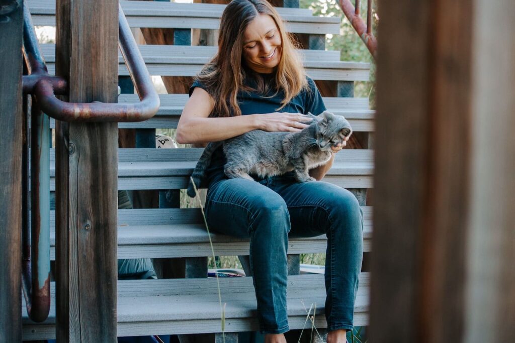 Eine Frau sitzt auf einer Treppe mit einer Katze auf dem Schoß, sie passt als Petsittern auf die Katze auf und ist bei Trustedhousesitters angemeldet