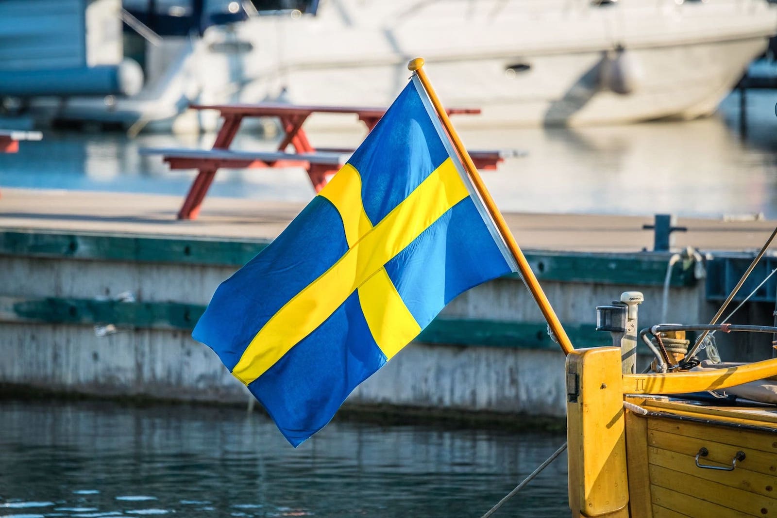 Eine schwedische Flagge auf einem Boot. Im Hintergrund sieht man ein Schiff. Von Deutschland kann man bequem mit der Fähre nach Schweden fahren, auch für Wohnmobile ist dies eine entspannte Überfahrt